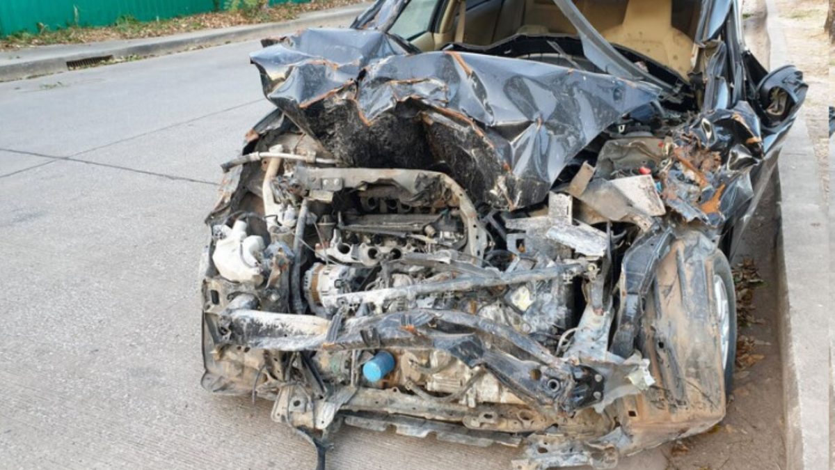 Carro preto com a frente completamente destruída após colisão, motor e estrutura expostos.