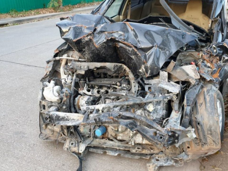 Carro preto com a frente completamente destruída após colisão, motor e estrutura expostos.