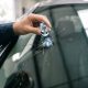 Mão segurando uma ferramenta de reparo/apontador de vidro enquanto acerta o centro da trinca no para-brisa de um carro.