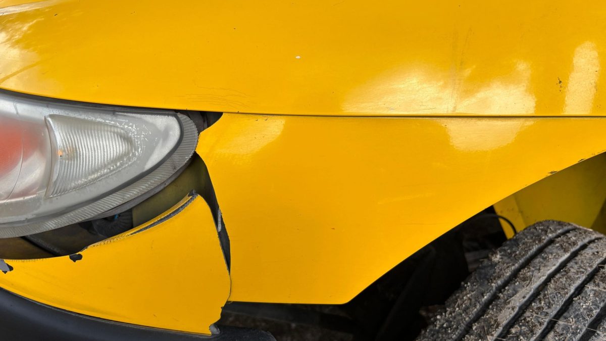 Para-choque dianteiro amarelo rachado e desalinhado próximo ao farol do veículo.