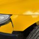 Para-choque dianteiro amarelo rachado e desalinhado próximo ao farol do veículo.