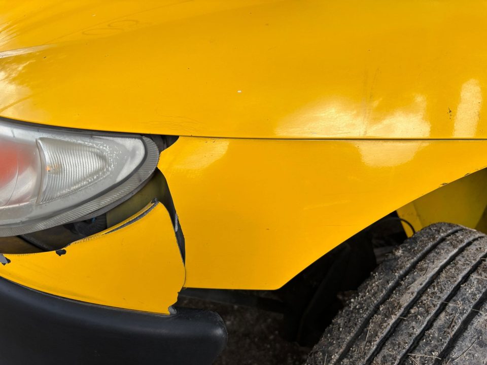 Para-choque dianteiro amarelo rachado e desalinhado próximo ao farol do veículo.
