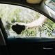 Imagem feita de dentro de um carro, focando no vidro lateral do motorista, que está molhado e com espuma e está sendo esfregado com um pano úmido